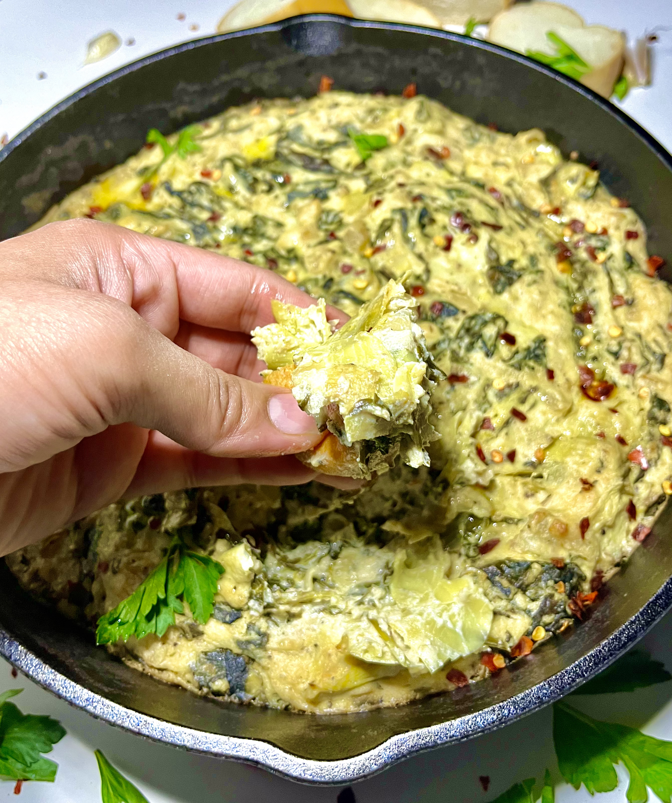 hand dipping bread into artichoke dip